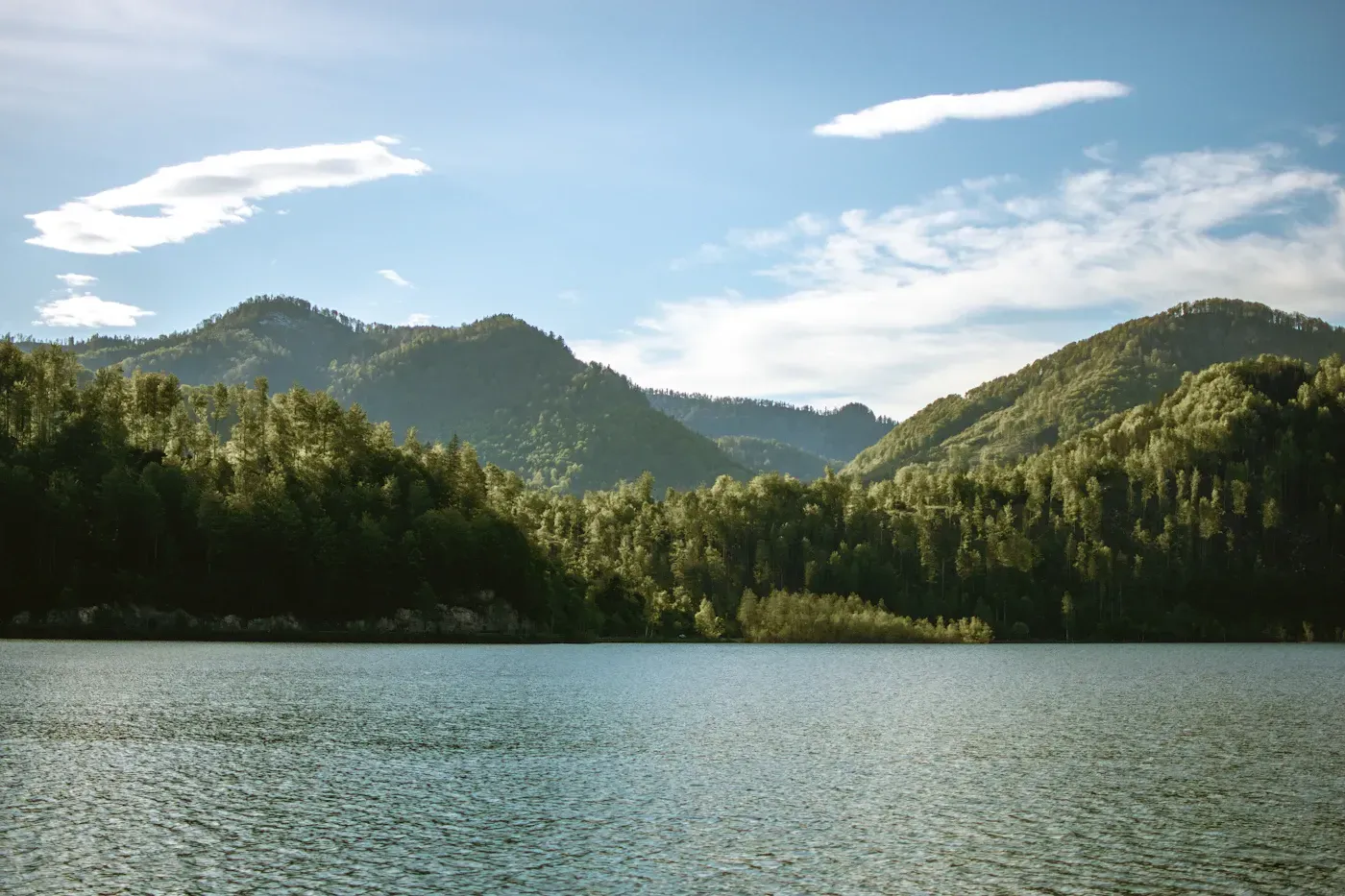 Forested mountains over a lake under passing clouds